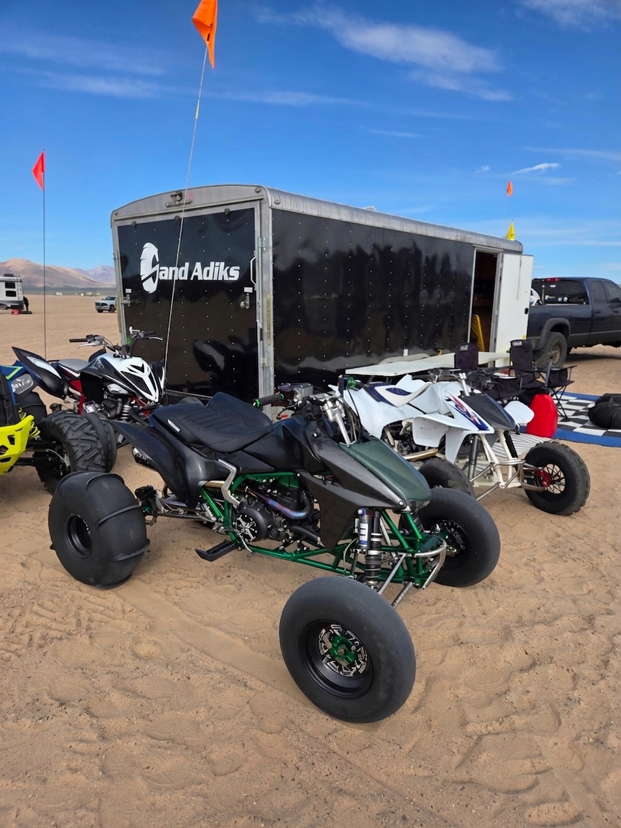 Sand Adiks logo sticker on a black trailer at the dunes with ATVs parked in the sand